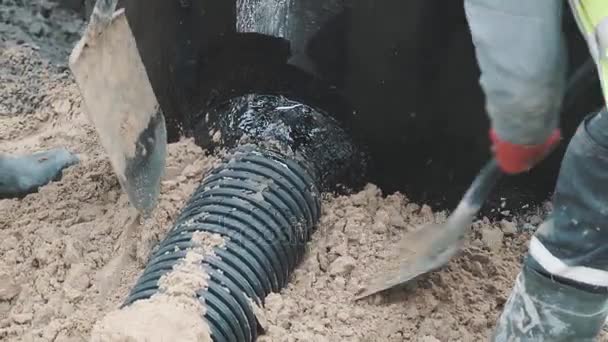 Två arbetare komprimera sand runt svart plaströr med spadar och stövlar — Stockvideo