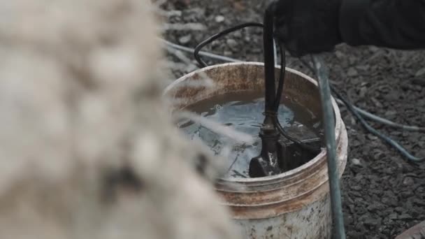 Hand in glove put industrial pump inside plastic bucket of dirty water — Stock Video