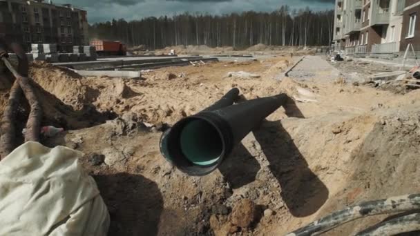 Dolly shot two long black plastic tubes laying in trench at building site — Stock Video