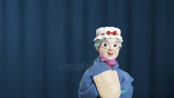 Aged woman hand puppet shakes head and actively break dances on blue background — Stock Video