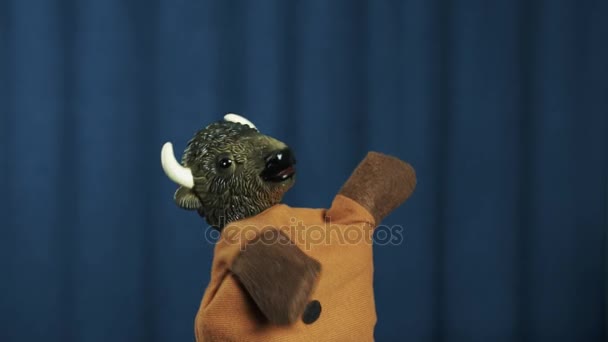 Marionnette à main de Buffle jouant de la guitare à air et secouant la tête sur scène avec un fond bleu 