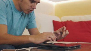 Kasalı tablete video oyunu oynarken kanepede oturan mavi tişörtlü dalmış adam