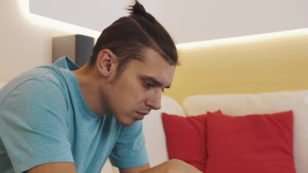 Koncentruje się człowiek w niebieską koszulę, siedząc na kanapie, grając gier wideo na tablecie obudowane — Wideo stockowe