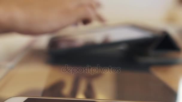 Cased tablet e smartphone em mesa de vidro usado por cara em camisa azul, falando — Vídeo de Stock