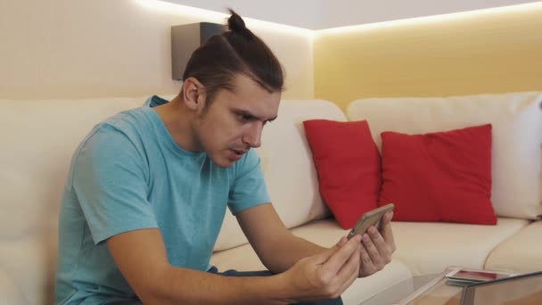 Homem alegre em camisa azul no sofá na sala de estar conversa vídeo chamada no smartphone — Vídeo de Stock