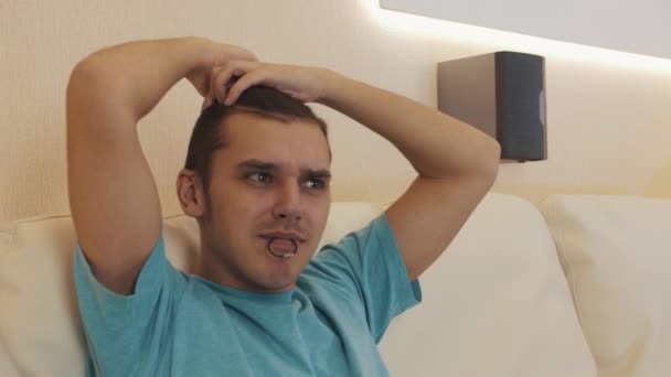 Man in blue shirt making hair knot sitting on white leather sofa in living room — Stock Video