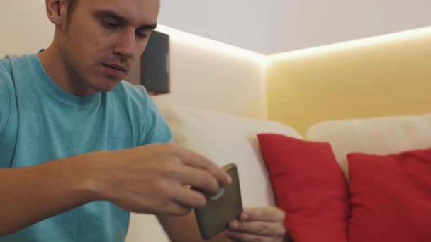 Fröhlicher Kerl im Wohnzimmer legt Smartphone auf den Tisch, startet Videoanruf, winkt — Stockvideo