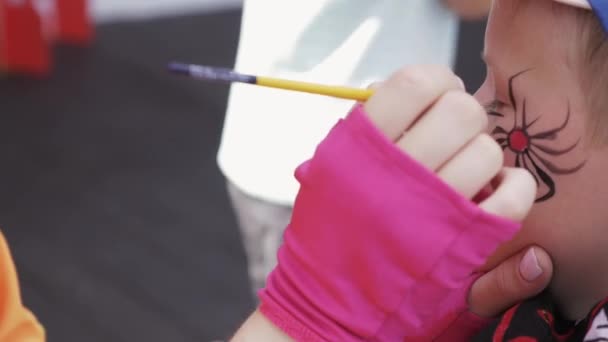 Vrouw in roze handschoenen verf gezicht van tiener jongen. Spin. Borstel. Zomerfestival — Stockvideo