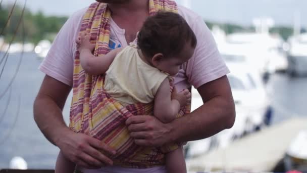 Il padre barbuto tiene il bambino in fionda sul lungomare. Evento. Estate giornata di sole . — Video Stock