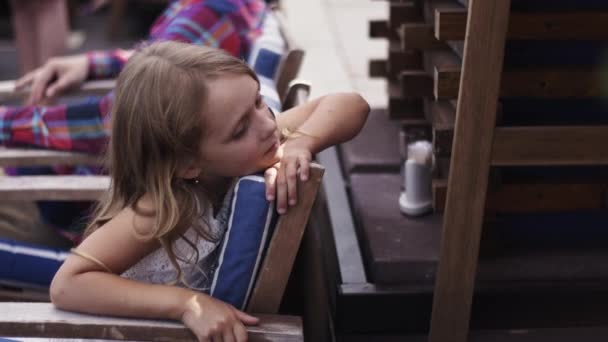 Teen flicka med målad blomma på kinden som sitter på restaurangens terrass. Sommar — Stockvideo