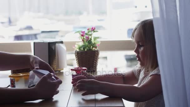 Matka učí malou holčičku papíru loď na terase restaurace. Tabulka. — Stock video