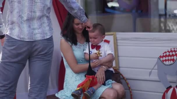 Mutter posiert mit kleinem Sohn in roter Fliege auf der Terrasse. Spielzeug. Fotograf — Stockvideo