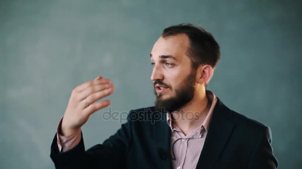 Бородатый мужчина в пиджаке и полосатой рубашке жестикулирует во время разговора на изолированной стене — стоковое видео