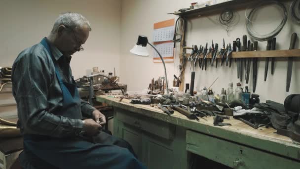 Meister in Brille und Schürze am Schreibtisch mit Teilen und Instrumenten in der Werkstatt — Stockvideo