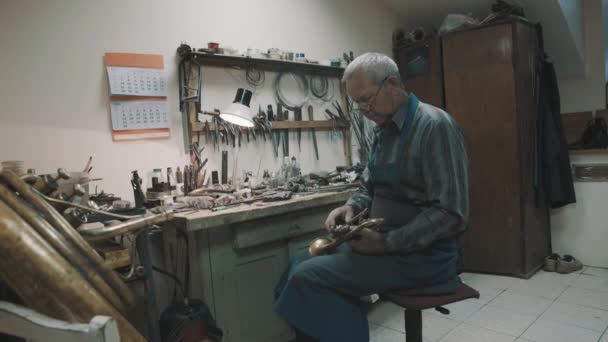 Мастер по очкам и фартуку работает с тубой и инструментами в мастерской — стоковое видео