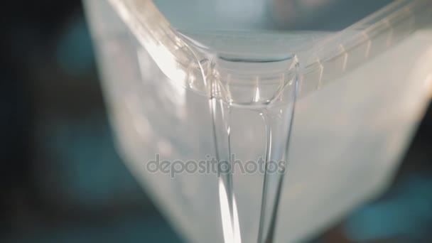 Liquido trasparente versando lentamente fuori contenitore di plastica trasparente quadrato — Video Stock