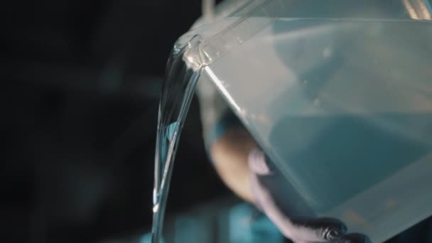 Mannenhand in rubberen handschoen gieten van water uit vierkant plastic container — Stockvideo