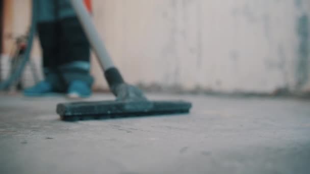 Hombre en bata de trabajador zapatos azules manguera de aspiradora de dirección sobre piso de hormigón — Vídeo de stock