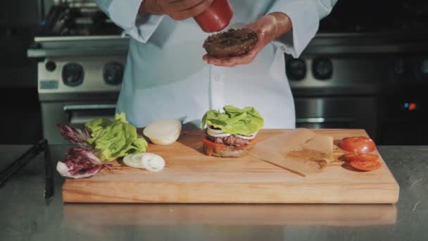 Chefe de cozinha em roupão branco fazendo hambúrguer, derrama ketchup no pão — Vídeo de Stock