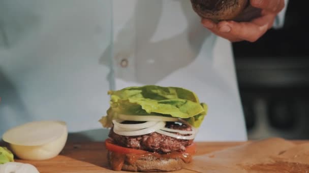 Male cooking chief in white robe finishes making hamburger and takes it in hands — Stock Video