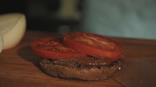 Male cooking chief in white robe making hamburger puts grilled meat on tomatoes — Stock Video