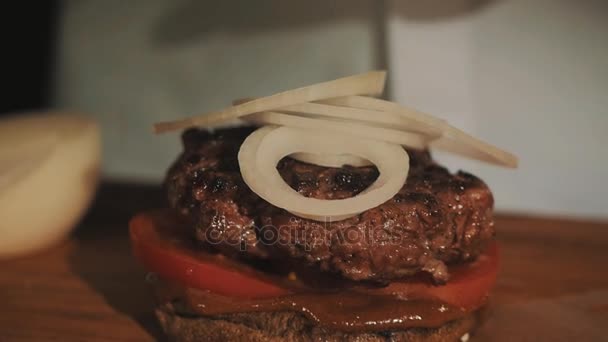 Chefe de cozinha masculino em roupão branco fazendo hambúrguer coloca salada verde na cebola — Vídeo de Stock