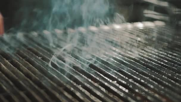 Cooking chief puts uncooked meat piece on hot smoking grill using forceps — Stock Video