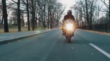 Motorcu açık siperliği ile kask içinde Şehir Parkı boyunca kameraya doğru Motosiklet sürmek