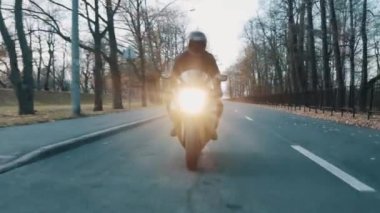 Motorcu kapalı siperliği ile kask içinde motosiklet park boyunca kameraya doğru sürmek