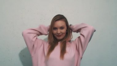 Kazak üzerine sevimli sarışın kız gülümseyen koyar hood ve beyaz duvara yatmak