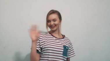 Gülümseyen ve beyaz arka plan üzerinde el sallayarak çizgili gömlekli güzel kız