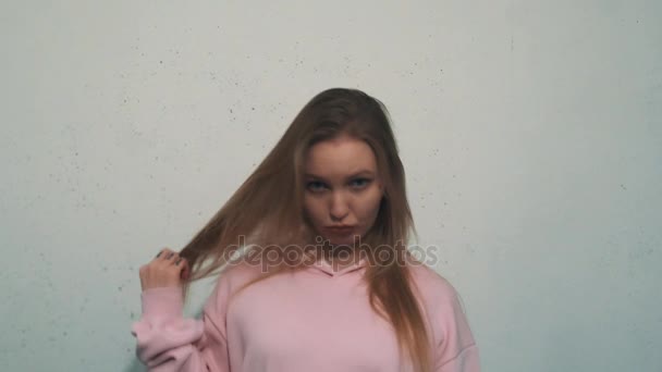 Jolie fille blonde avec des tatouages en sweat-shirt rose tord les cheveux et mord la lèvre — Video