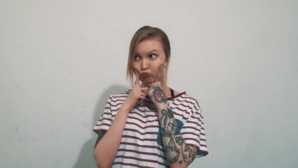 Aranyos szőke lány csíkos póló tetoválás tegye ujjait a fújt arca — Stock videók