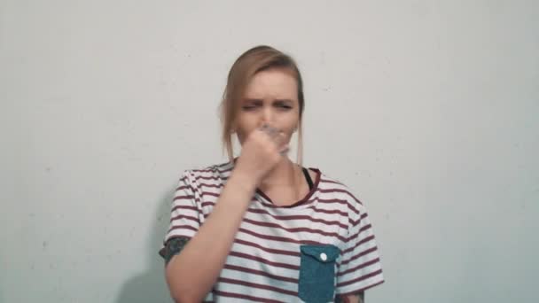 Linda chica rubia con camisa a rayas, huele algo horrible y cubre la nariz — Vídeo de stock