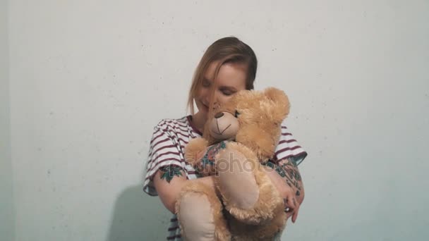 Mujer rubia linda en camisa a rayas con tatuajes, abrazos con juguete de oso de peluche — Vídeos de Stock
