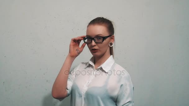 Mujer atractiva en los expansores de oreja camisa blanca mira en la cámara sobre gafas — Vídeos de Stock