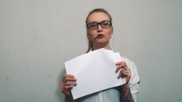 Attraktive Frau im weißen Hemd, mit Ohrenfleischtunneln, die Blatt Papier essen — Stockvideo
