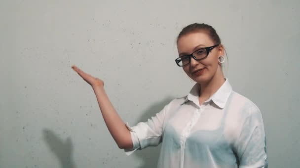 Привлекательная женщина в белой рубашке, с ушными туннелями, указывающими на белую стену — стоковое видео
