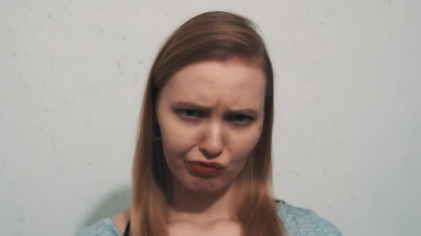Grumpy gadis muda kemeja abu-abu dengan terowongan telinga merajuk di depan dinding putih — Stok Video
