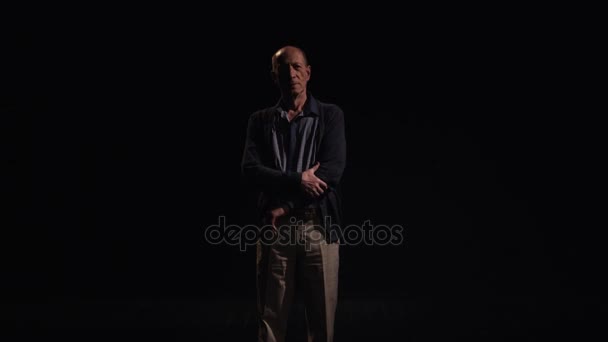 Elderly bald grey haired caucasian man rub chin and stands akimbo in black room — Stock Video