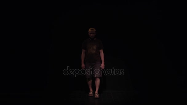 Young caucasian bearded man in yellow cap slowly walks in black room — Stock Video