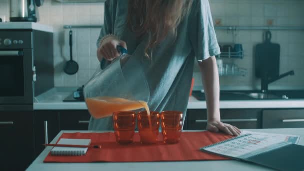 Tollpatschiges brünettes Mädchen gießt Orangensaft in rotes Glas und verschüttet es überall — Stockvideo