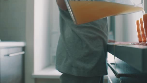 Zijaanzicht van de jonge vrouw sap van kruik gieten in glas, het morsen van vloeistoffen op tafel — Stockvideo