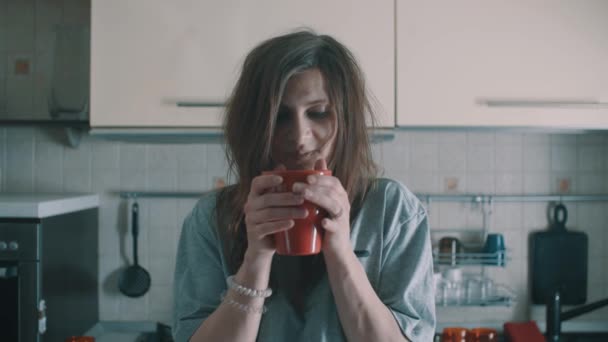 Mujer atractiva bebiendo café fuera taza roja y sonrisas en la cocina por la mañana — Vídeo de stock