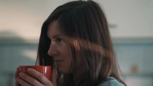 Attractive girl drinking coffee out red mug and winces in kitchen at morning — Stock Video