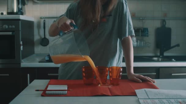 Sluggish brunette girl pouring orange juice into red glass, spills it everywhere — Stock Video