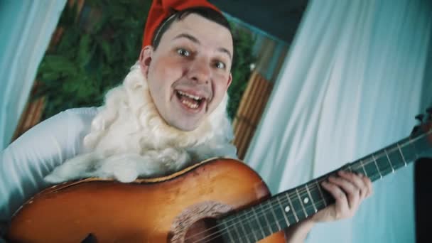 Веселий чоловік, одягнений як бородатий карлик танцює і грає на акустичній гітарі — стокове відео