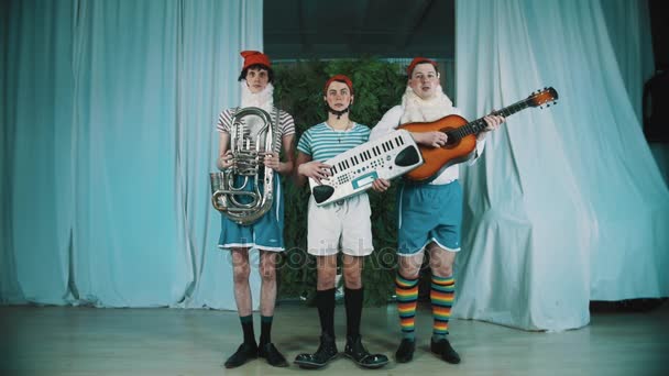 Three men dressed as gnomes with musical instruments jumps and playing music — Stock Video