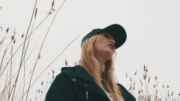 Młody atrakcyjny Blondynka w czarny żakiet i czapka stoi w trzcinach — Wideo stockowe