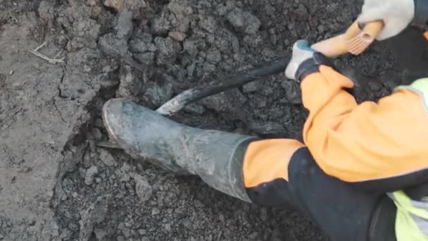 Worker in orange hard hat digging dirt up on breakstone with shovel in ditch — Stock Video